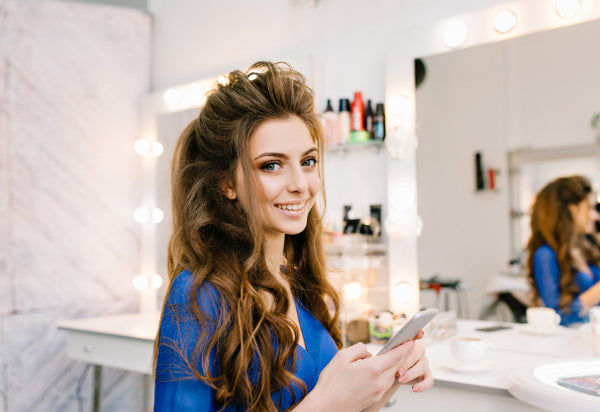 junge hübsche Frau lächelt in die Kamera während sie in einem Salon zurecht gemacht wird 